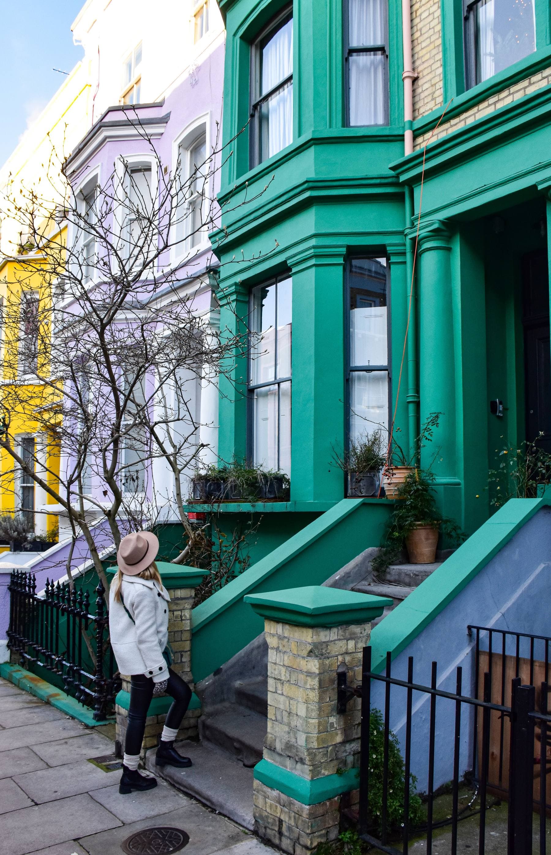 A young woman on the front steps of a colourful painted terrace in Notting Hill.